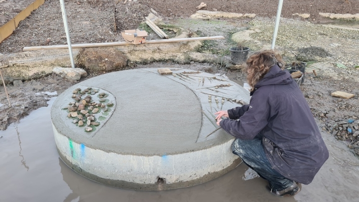 A person bent down drawing shapes in cement on a giant plinth.